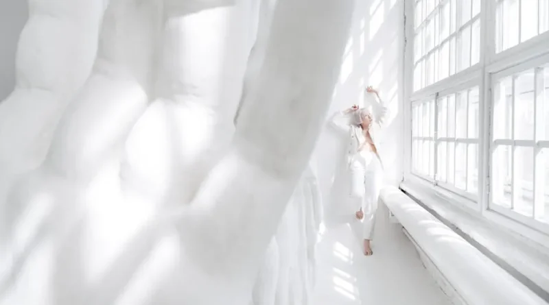 A stylish individual standing in a sunlit loft wearing a tailored blazer and relaxed denim