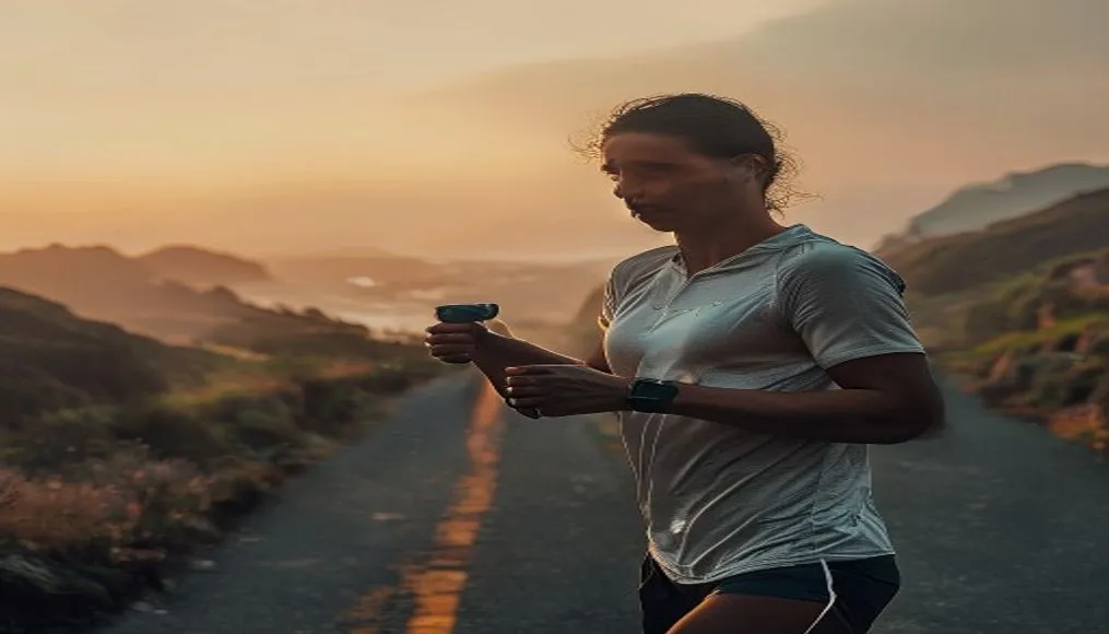 A runner checking their smartwatch while training on a scenic coastal road at dawn